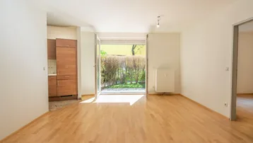 Helles Wohnzimmer mit Parkettboden, Zugang zum Garten und offener Verbindung zur Küche.