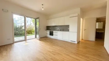 Heller offener Wohnbereich mit moderner Einbauküche, Holzboden und Zugang zur Terrasse.