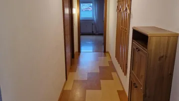 Langer Flur mit gemustertem Bodenbelag und Garderobe, der zu weiteren Räumen führt.