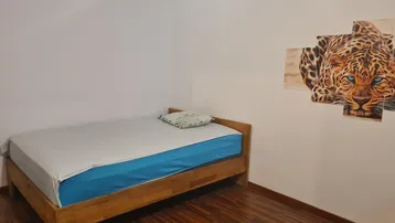 Einfaches Schlafzimmer mit Holzbett, Holzboden und einem auffälligen Leopardengemälde an der Wand.