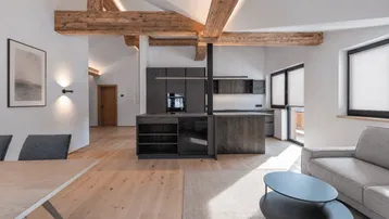 Offener Wohn- und Essbereich mit moderner Küche, Holzbalken und hellem Parkettboden.