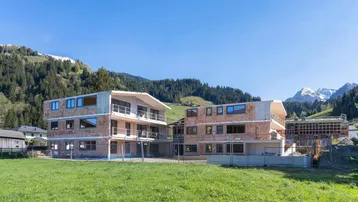 Zwei im Bau befindliche Gebäude mit Blick auf die umliegende Berglandschaft und grüne Wiesen.