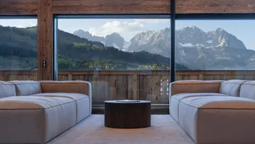 Helles Wohnzimmer mit großen Panoramafenstern, die einen atemberaubenden Bergblick bieten und viel natürliches Licht hereinlassen.