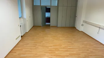 Geräumiger Büroraum mit hellem Laminatboden, weißen Wänden und integrierten Schränken, ideal für verschiedene Nutzungen.