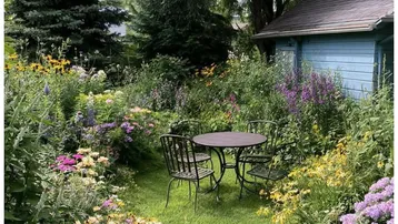 Idyllischer Garten mit üppigen Blumenbeeten, Rasenfläche und gemütlicher Sitzgelegenheit im Freien.