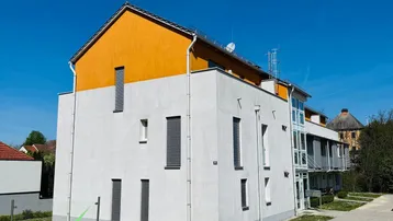 Modernes Mehrfamilienhaus mit weißer Fassade und orangefarbenem Dach unter blauem Himmel.