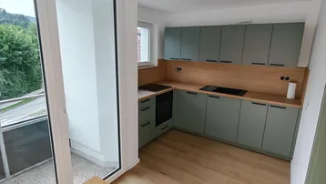 Moderne Küche mit hellgrünen Schränken, Holzarbeitsplatte und Zugang zum Balkon mit Bergblick.