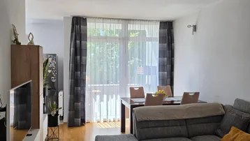Heller Wohn- und Essbereich mit bequemer Couch, Holzboden und Zugang zu einem Balkon durch große Fenster.