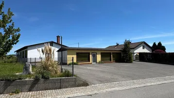 Außenansicht des Gebäudekomplexes mit großem gepflasterten Vorplatz unter blauem Himmel.