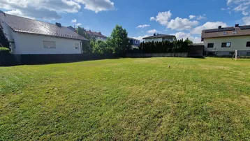 Großes, sonniges Grundstück mit Rasenfläche und umliegenden Wohnhäusern unter blauem Himmel.