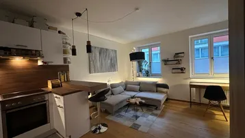 Moderner offener Wohnbereich mit integrierter Küche, Holzboden und gemütlichem Sofa am Fenster.