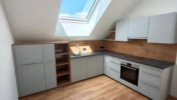 Moderne Küche im Dachgeschoss mit hellgrauen Schränken, Holzakzenten und großem Dachfenster.