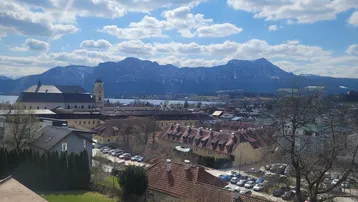 Panoramablick über die Stadt, einen See und majestätische Berge unter blauem Himmel.