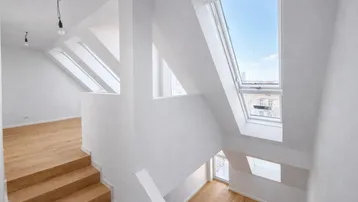Lichtdurchfluteter Treppenbereich im Dachgeschoss mit großen Dachfenstern und Holztreppe.
