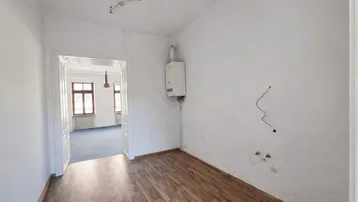 Leerer Raum mit Laminatboden, weißen Wänden und einem Gasboiler an der Wand.