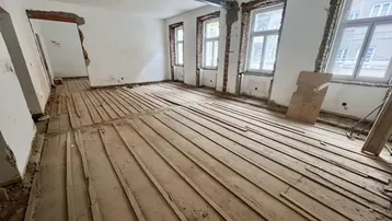 Großer Raum im Rohbauzustand mit freigelegten Holzdielen und sichtbaren Stahlträgern, bereit für die Renovierung.