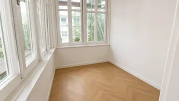 Helles Zimmer mit Fischgrätparkett und vielen Fenstern, ideal als Wintergarten oder Büro.