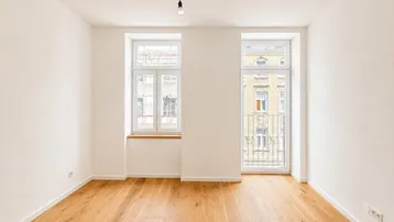 Helles Zimmer mit neuem Parkettboden, weißen Wänden und Zugang zu einem französischen Balkon.