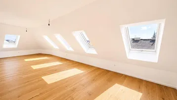Heller Dachgeschossraum mit schrägen Wänden, Holzboden und mehreren Dachfenstern, die viel Licht hereinlassen.