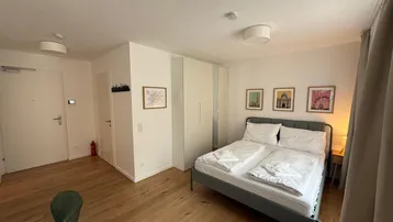 Helles Schlafzimmer mit Holzboden und modernen Möbeln in einem offenen Wohnbereich.