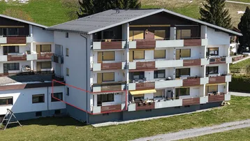 Mehrfamilienhaus mit mehreren Balkonen und Blick auf die umliegende grüne Landschaft.