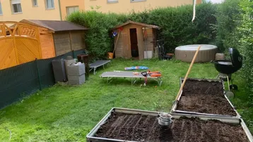 Gepflegter Gartenbereich mit Rasenfläche, Hochbeeten, Gartenhaus und aufblasbarem Whirlpool.