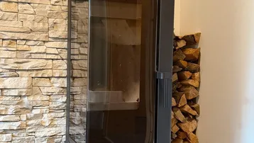 Moderner Holzofen vor einer Steinwand mit gestapeltem Brennholz, schafft eine gemütliche Atmosphäre.