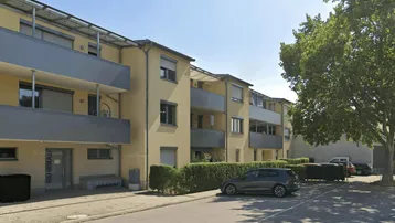 Mehrfamilienhaus mit gelber Fassade, Balkonen und Photovoltaikanlage auf dem Dach.