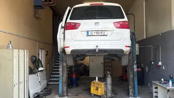 Geräumige Werkstatt mit einem weißen Auto auf einer Hebebühne, umgeben von Arbeitsgeräten und einem Betonboden.