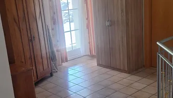 Heller Flur mit Fliesenboden, zwei Kleiderschränken und Zugang zu einer Treppe.