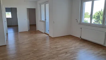 Helles Wohnzimmer mit Parkettboden, großen Fenstern und Zugang zum Balkon.