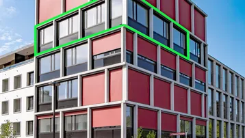 Modernes Gebäude mit roten Fensterläden und großen Fenstern in städtischer Umgebung.