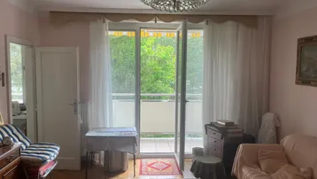 Helles Wohnzimmer mit traditionellem Teppich, Kronleuchter und Zugang zum Balkon.