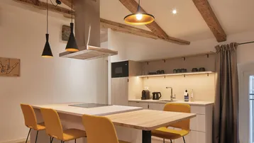 Moderne Küche mit Kochinsel, Barhockern, integrierten Geräten und rustikalen Holzbalken an der Decke.