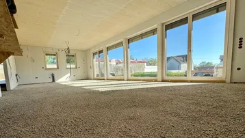 Helles Zimmer im Rohbau mit großen Fenstern und Blick ins Grüne, bereit für den Innenausbau.