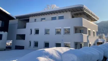Modernes Mehrfamilienhaus mit weißer Fassade und schneebedecktem Dach in winterlicher Landschaft.