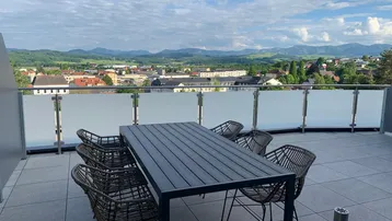 Geräumige Dachterrasse mit Esstisch, Sitzgelegenheiten und weitem Blick auf die umliegende Landschaft und Berge.