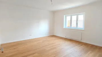 Helles, leeres Zimmer mit Holzboden und weiß gestrichenen Wänden, bereit zur individuellen Gestaltung.