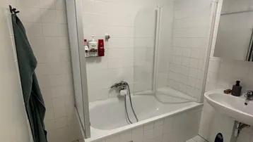 Helles Badezimmer mit Badewanne, Duschabtrennung und Fenster, ausgestattet mit weißen Fliesen.