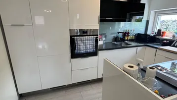 Moderne Küche mit weißen Hochglanzfronten, integriertem Backofen und dunkler Arbeitsplatte.