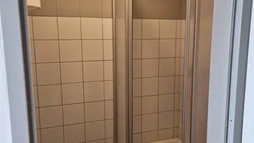 Kleines Badezimmer mit Duschkabine und weiß-grauen Fliesen an den Wänden.