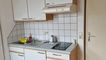 Kleine Küchenzeile mit weißen Schränken, Spüle und Induktionskochfeld.