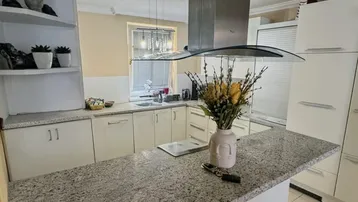 Helle Küche mit Kücheninsel, Granitarbeitsplatte und integrierter Dunstabzugshaube.