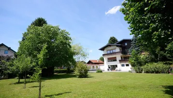 Großzügiger Gartenbereich mit gepflegtem Rasen und Blick auf das Wohnhaus unter blauem Himmel.