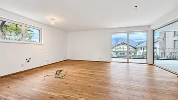 Heller Wohnbereich mit Holzboden, großen Fenstern und Zugang zu einer Terrasse mit Bergblick.