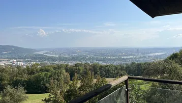 Panoramablick von einem Balkon über eine weite Landschaft mit Fluss und Stadt im Hintergrund.