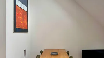 Heller Essbereich mit Holztisch, modernen Kunstwerken und Dachfenstern unter einer schrägen Decke.
