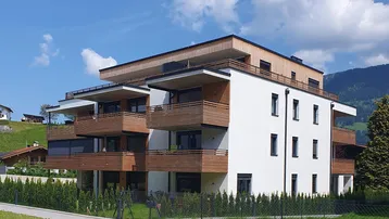 Modernes Mehrfamilienhaus mit Holzfassade, Balkonen und grüner Umgebung vor Bergkulisse.