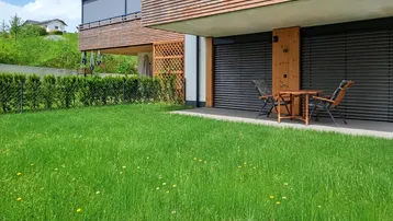 Gepflegter Gartenbereich mit Rasenfläche und kleiner Terrasse vor dem modernen Gebäude.