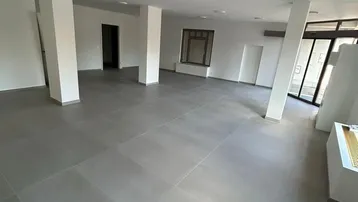 Geräumiger, heller Gewerberaum mit modernen grauen Fliesen und vielen Fenstern, ideal für Büros oder Einzelhandel.